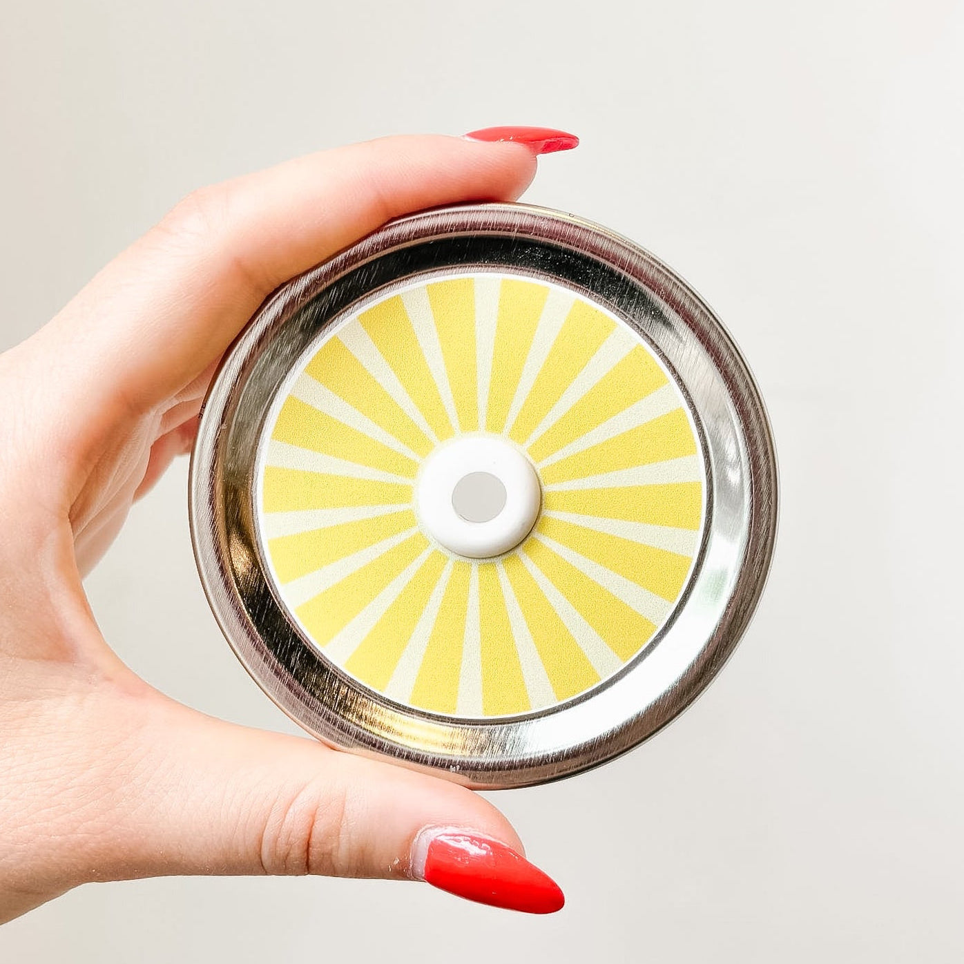 Hand holding a mason jar patterned straw lid that has yellow striped design