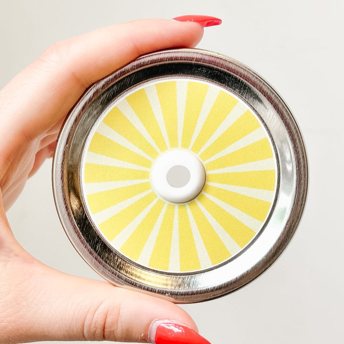 Hand holding a mason jar patterned straw lid that has yellow striped design