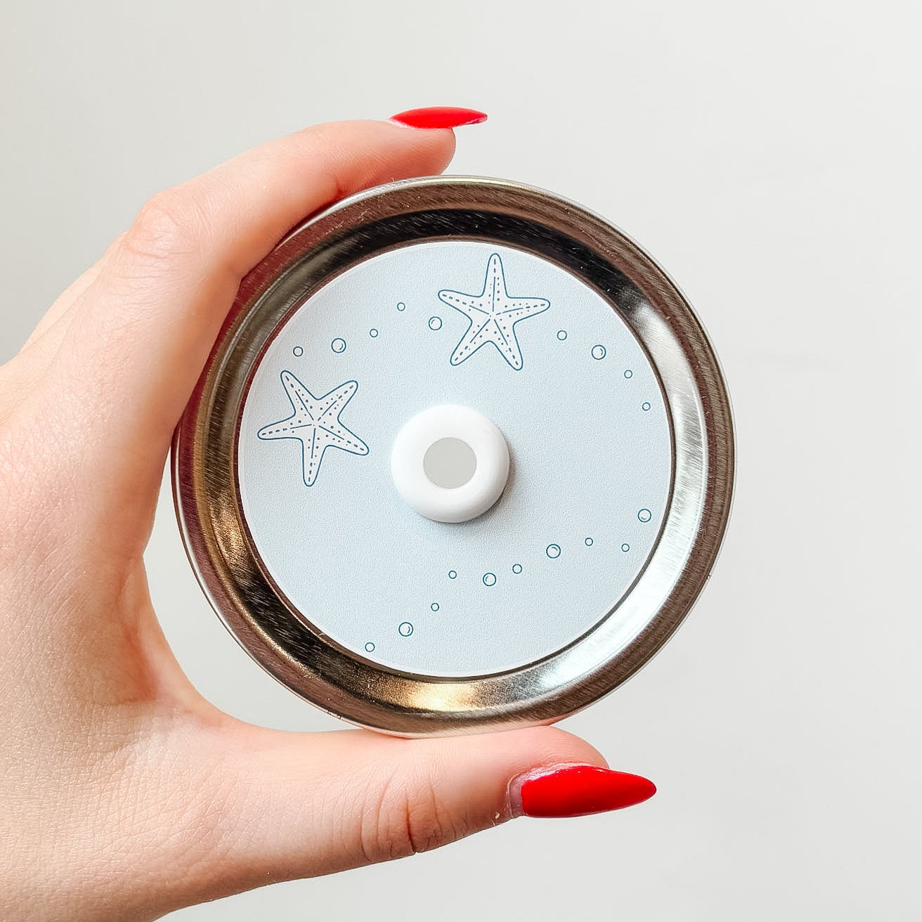 Hand holding mason jar patterned straw lid up close that has starfish and bubbles on light pastel blue background