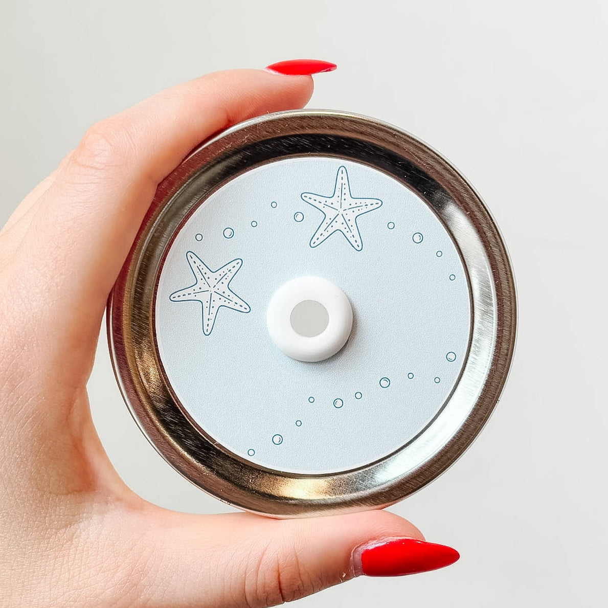 Hand holding mason jar patterned straw lid up close that has starfish and bubbles on light pastel blue background