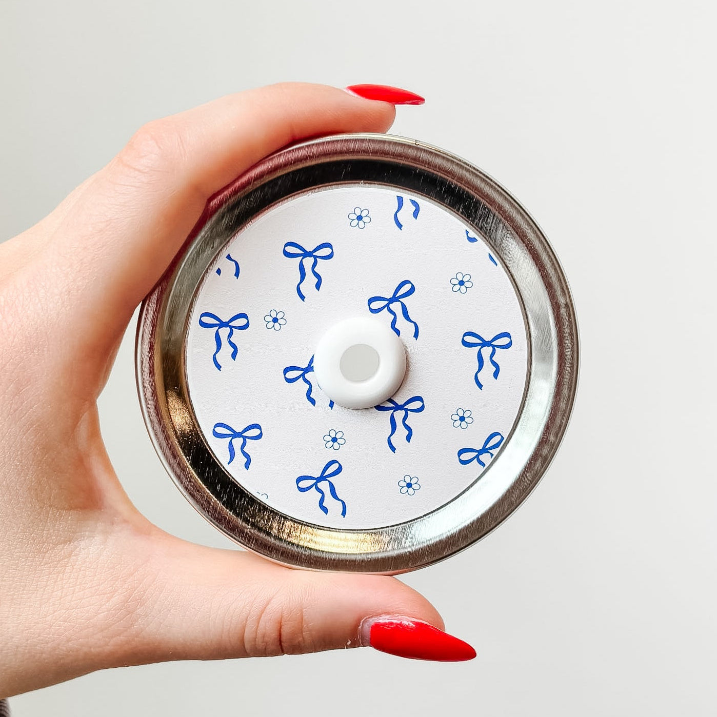Hand holding a mason jar patterned straw lid up close that has blue bows and flowers on white background