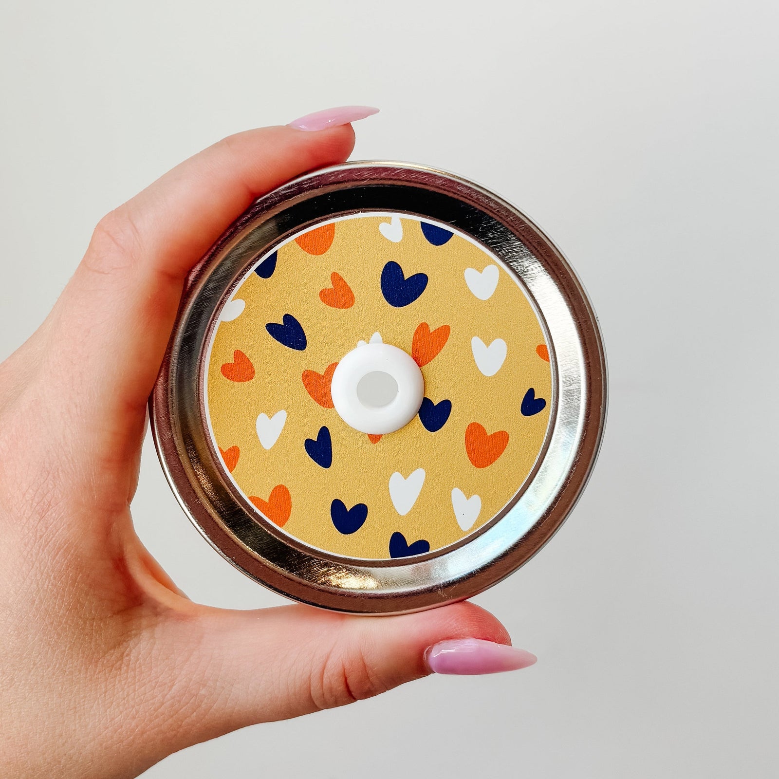Hand holding mason jar patterned straw lid that has navy, white and orange hearts on light orange background.