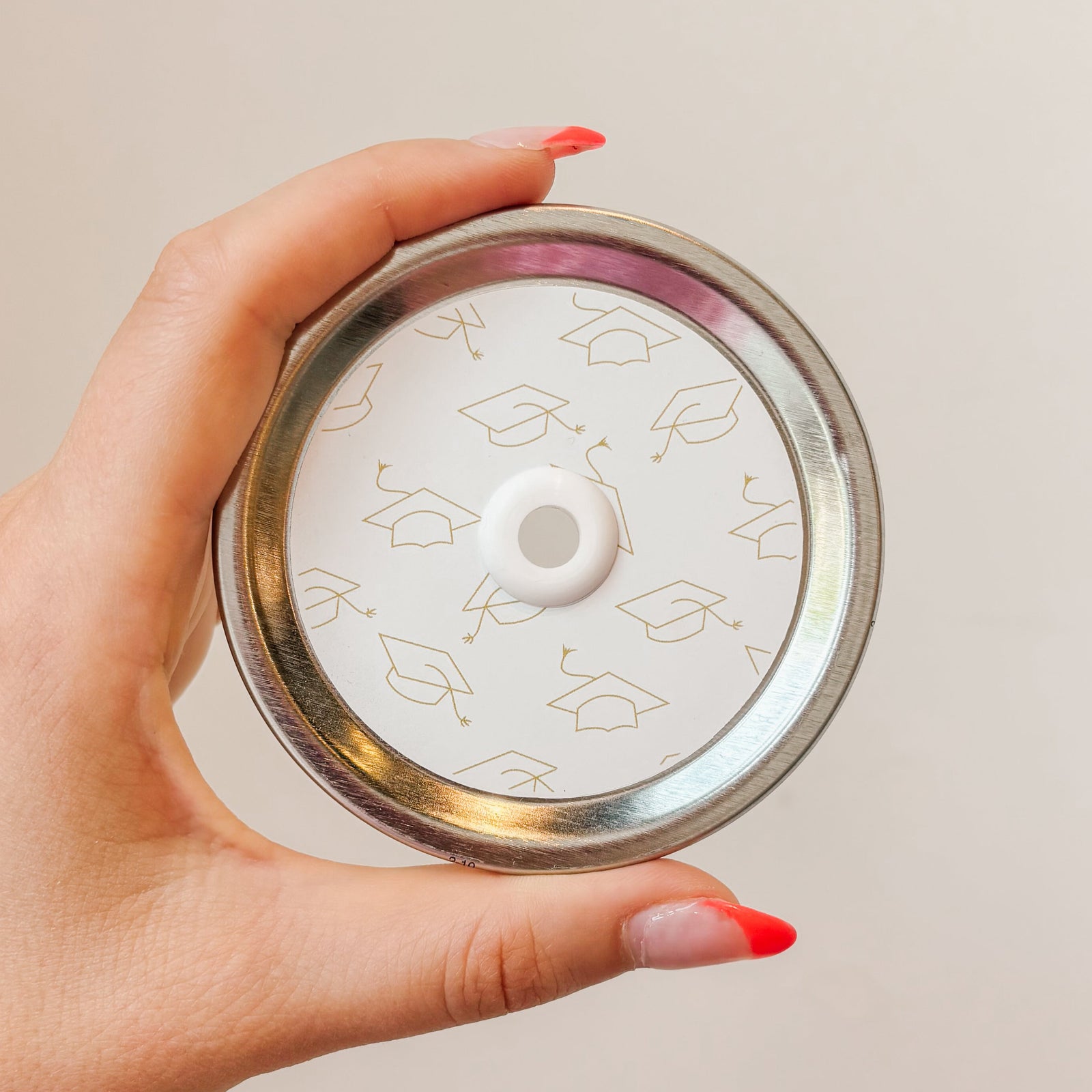 Hand holding mason jar patterned straw lid that has gold grad caps on white background