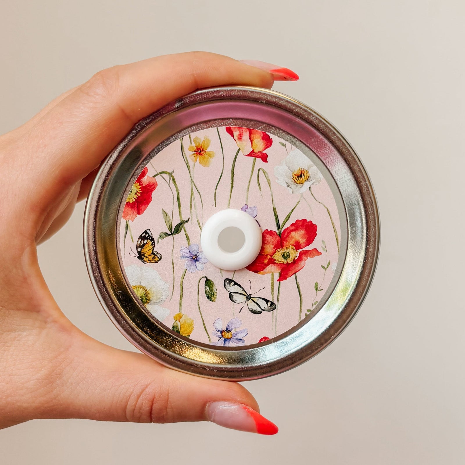straw lid with a pink background, there are green stems/leaves taking up most of the centre of the lid, there are also flowers and butterflies scattered