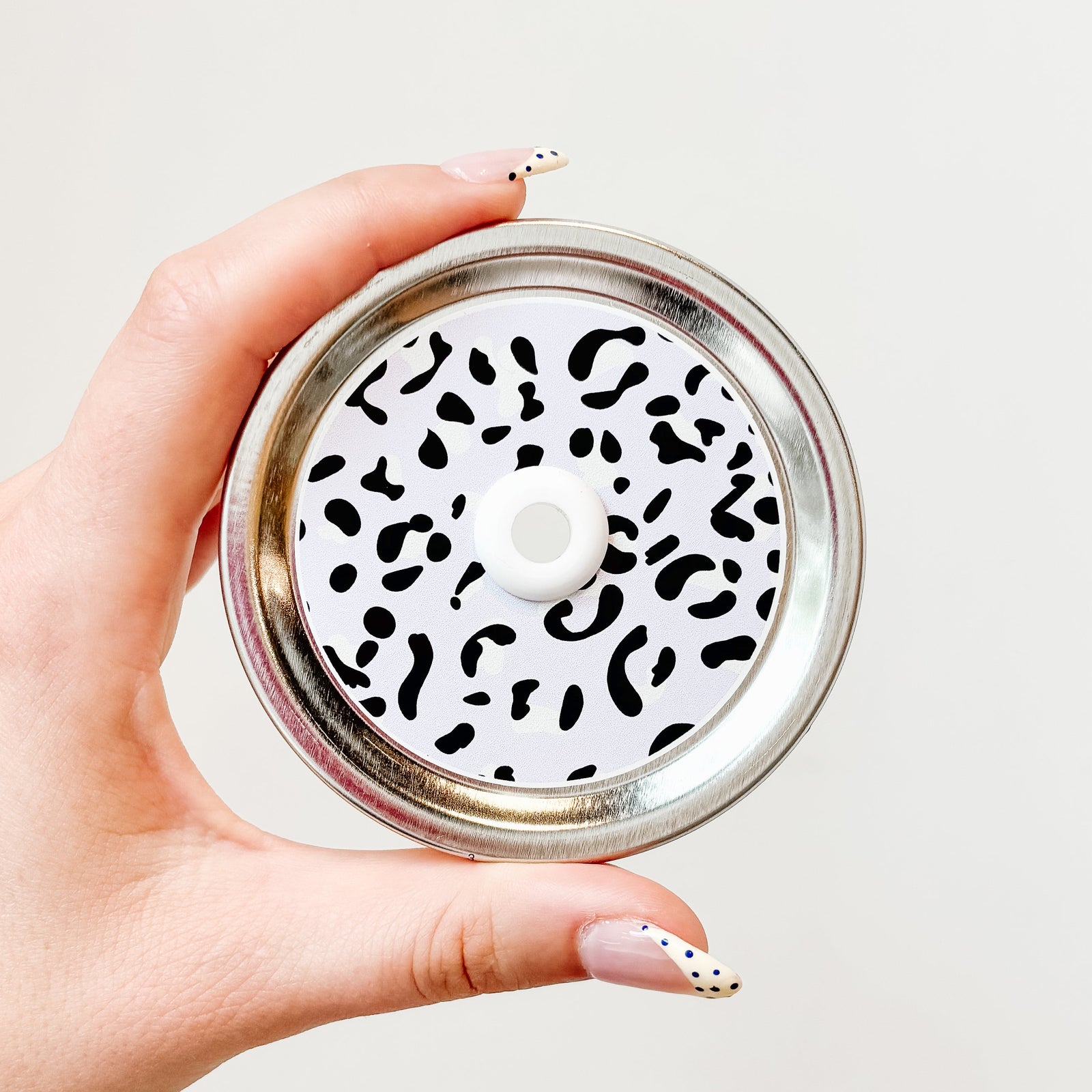 Hand holding a lavender leopard print patterned mason jar straw lid with white straw grommet