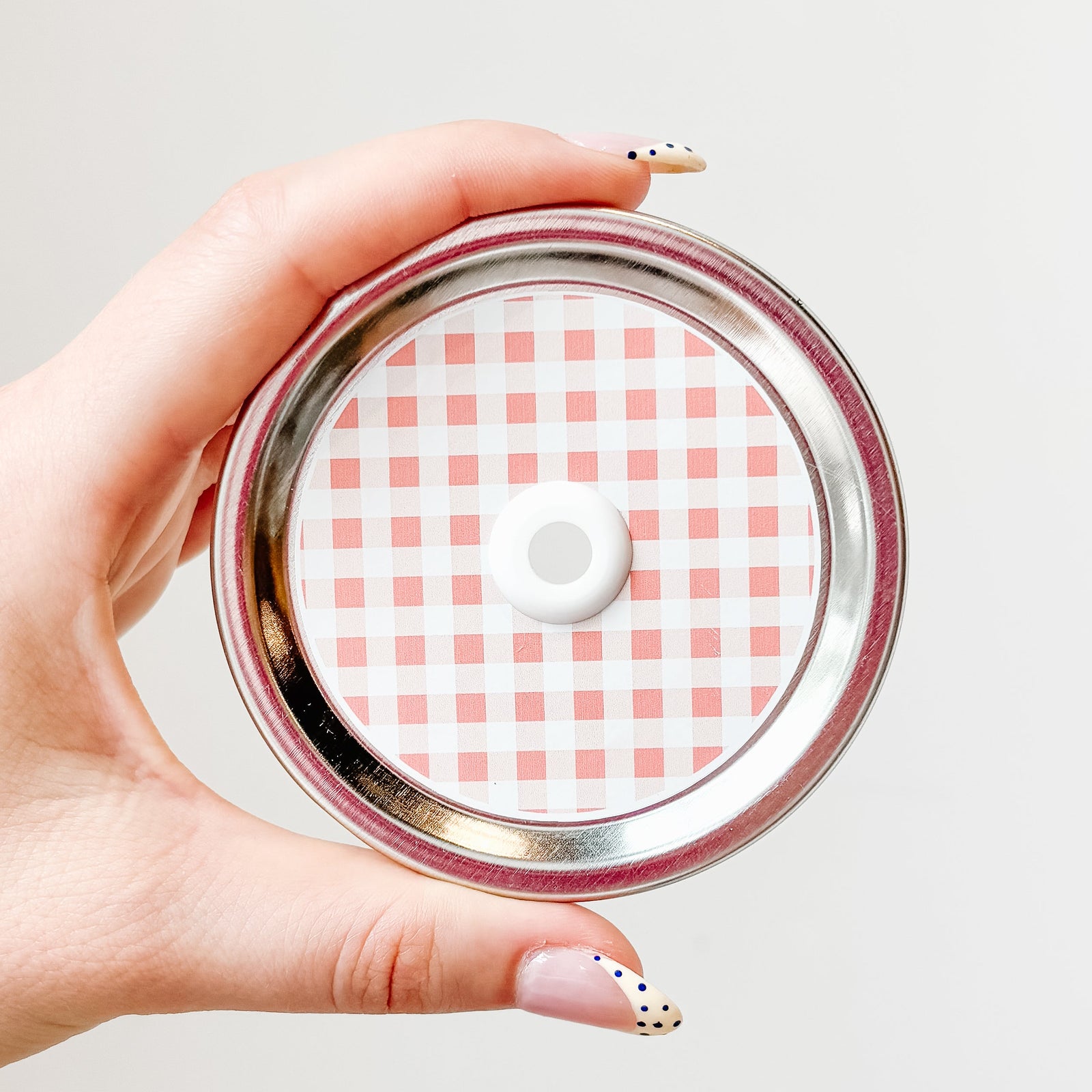 Hand holding mason jar straw lid that is peach and white gingham design