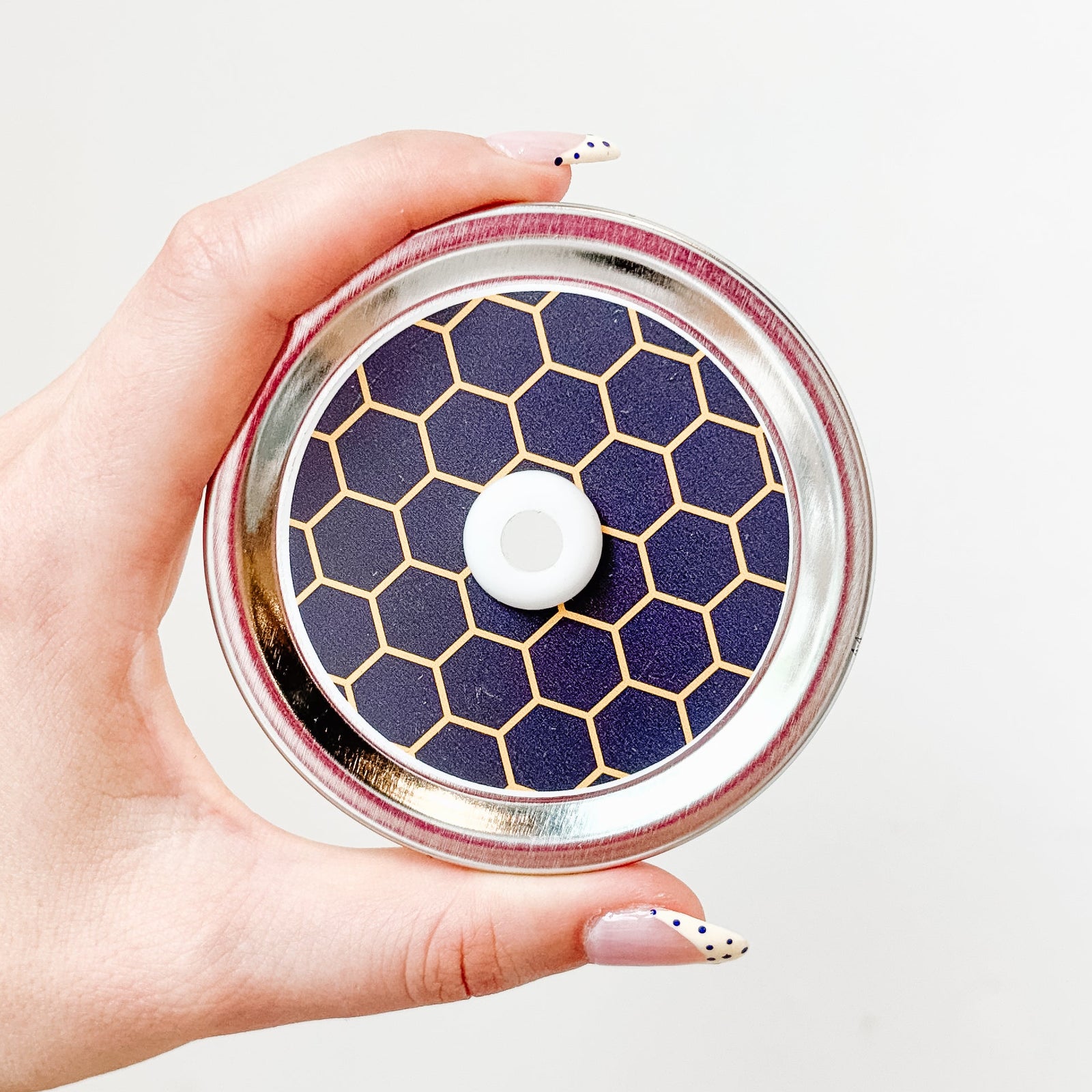 Hand holding mason jar straw lid that is a black and yellow honeycomb design