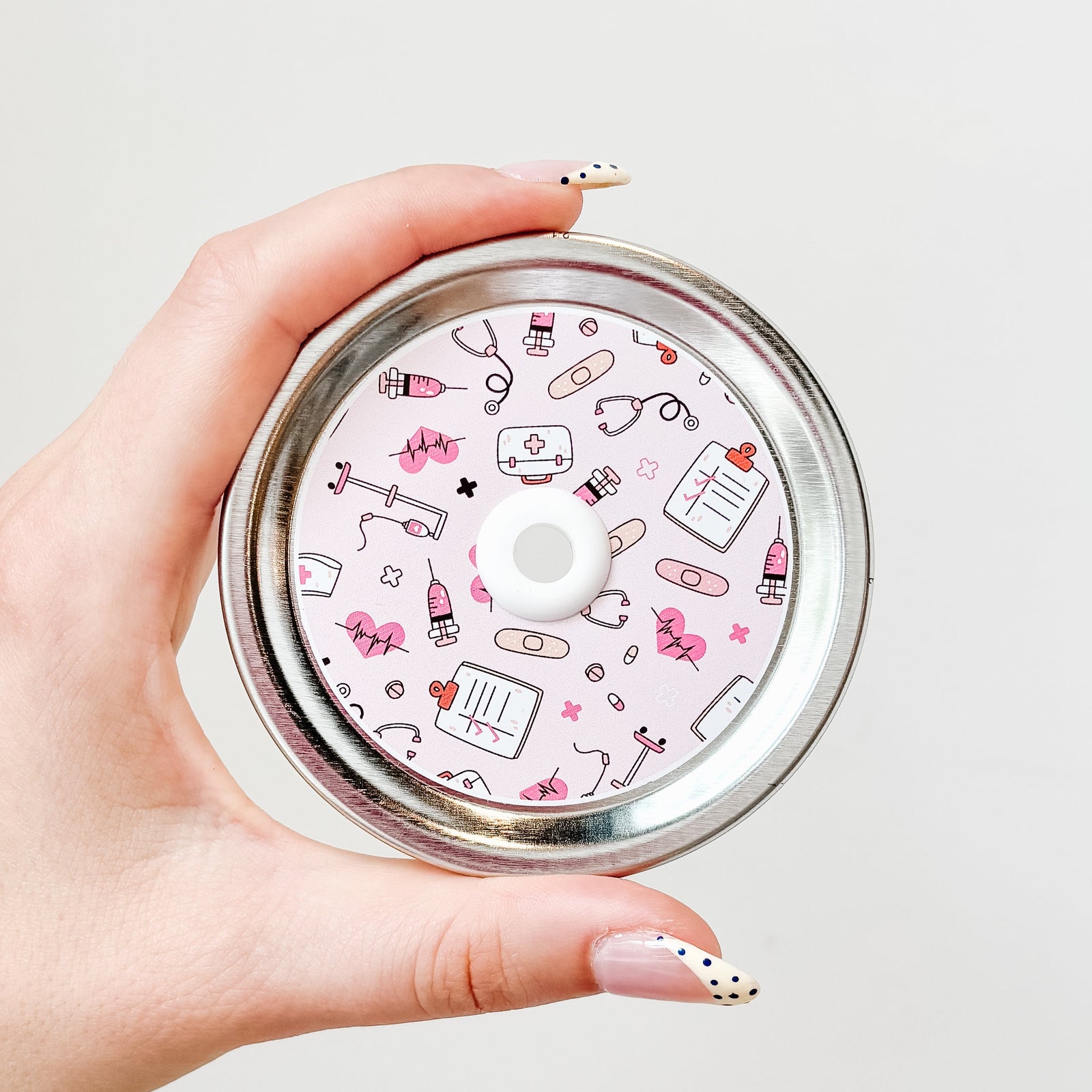 straw lid with light pink background and stethoscopes, needles, IV poles, checklists, bandaids, and pills scattered across