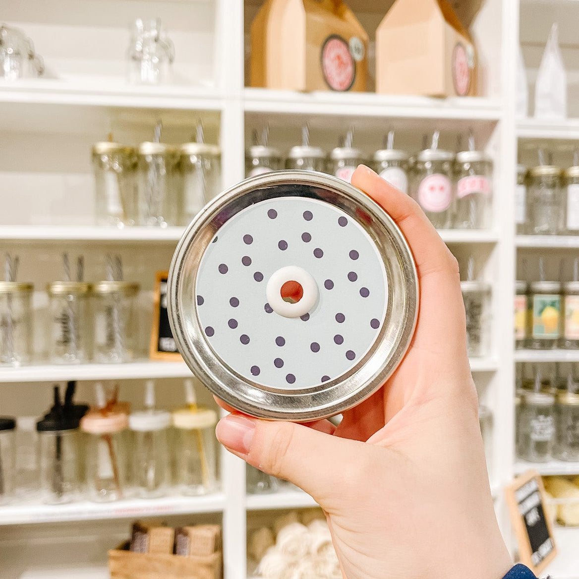 Hand holding a patterned mason jar straw lid that has navy polka dots on a minty blue background.