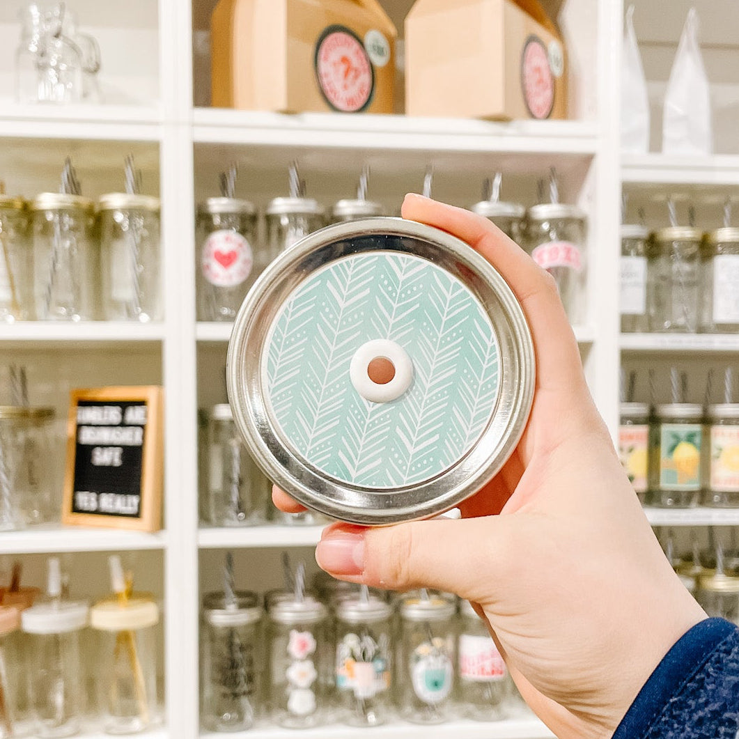 Hand holding a mason jar patterned straw lid with white boho style chevron pattern on a light aqua background.