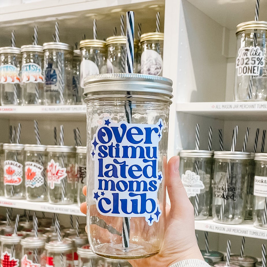 Hand holding a mason jar tumbler that reads overstimulated moms club in dark and light purple