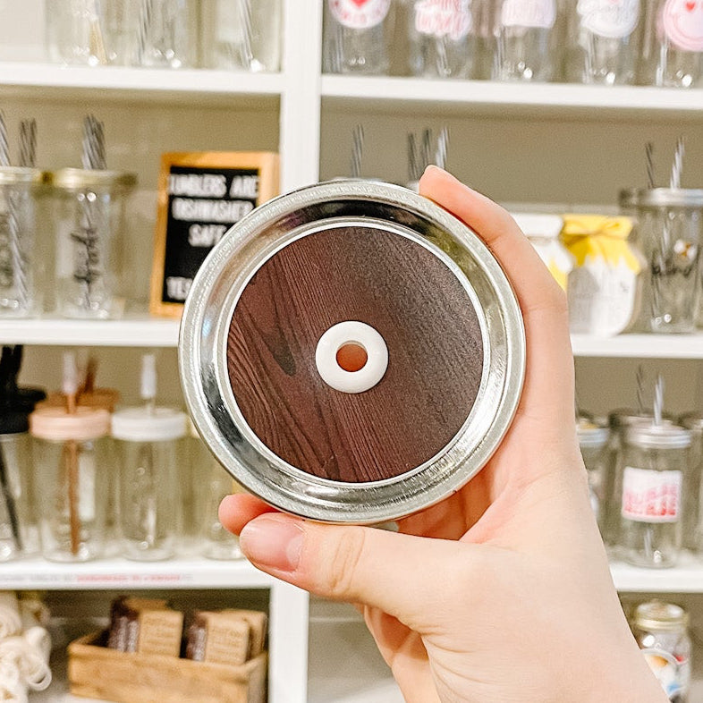 Hand holding a mason jar patterned straw lid that has a dark brown wood design.