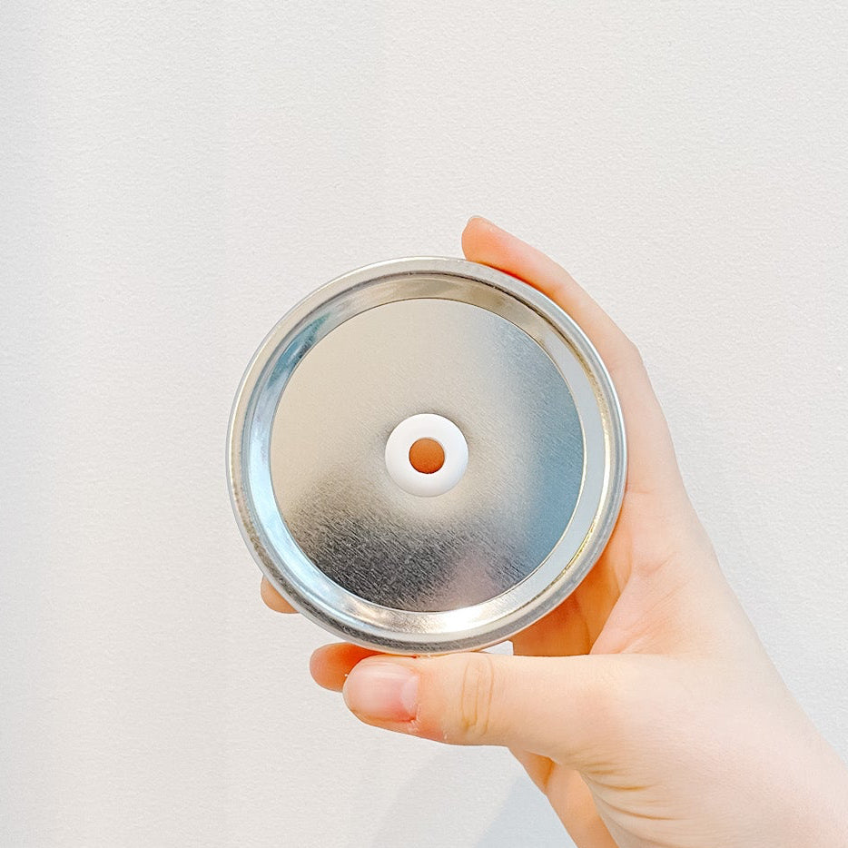 Hand holding a plain silver mason jar straw lid on a white background