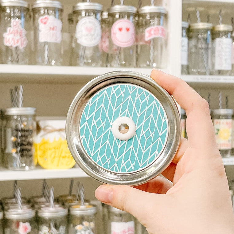 Hand holding mason jar patterned straw lid that has a white fine line chevron type pattern on blue background