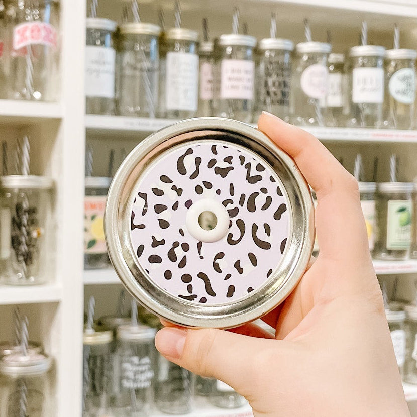 Hand holding mason jar patterned straw lid that is cheetah print on lavender background