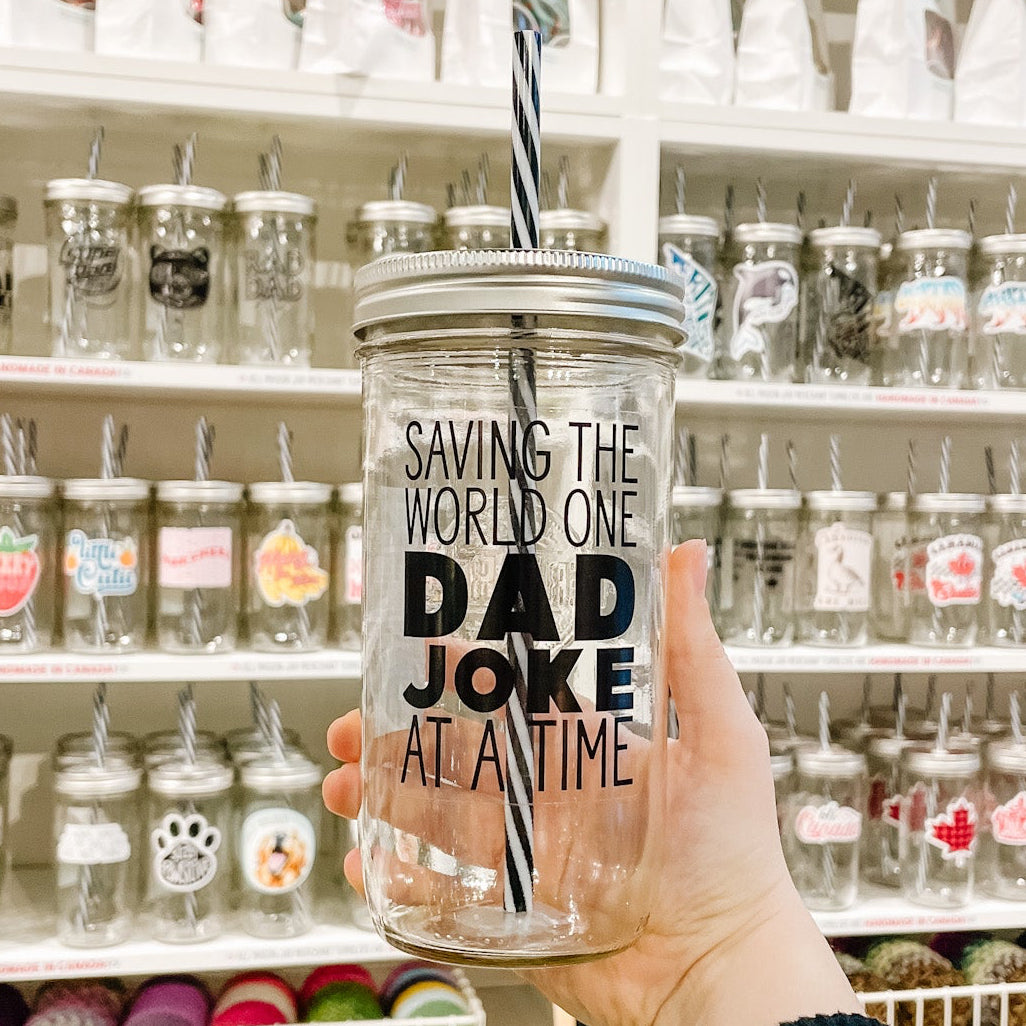 Hand holding mason jar tumbler that reads saving the world one dad joke at a time in black ink on clear