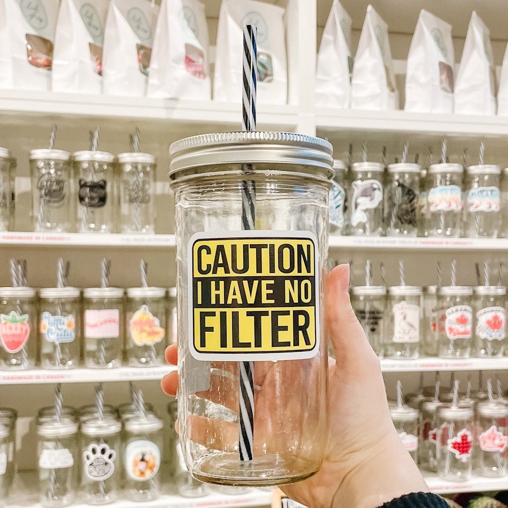 Hand holding mason jar tumbler that reads caution i have no filter in black text on black and yellow background