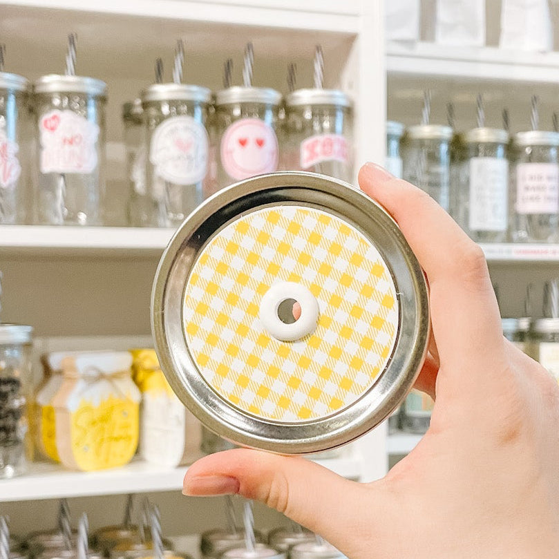 Hand holding mason jar patterned straw lid that is white and yellow gingham print
