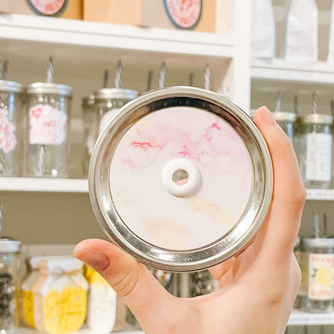 Tumbler with water and a sticker that has a pink, peach, and white hibiscus flowers. Photographed as a flat lay in a winnowing tray with palm leaves.