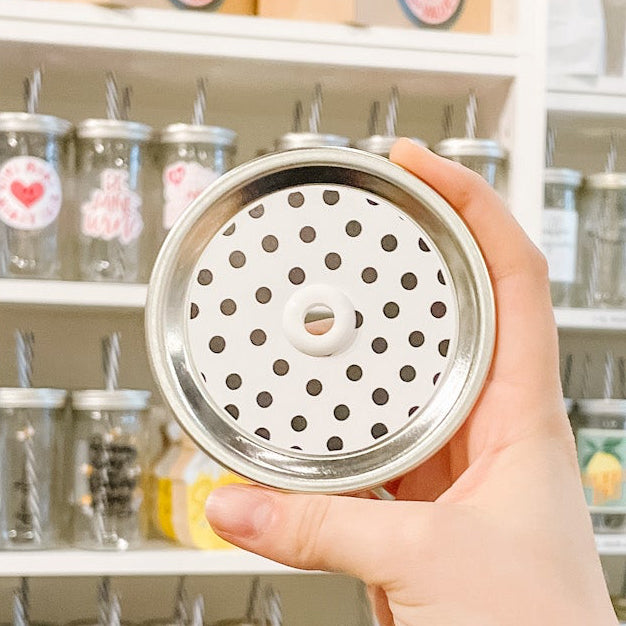 Hand holding mason jar patterned straw lid that has black polka dots on white background.