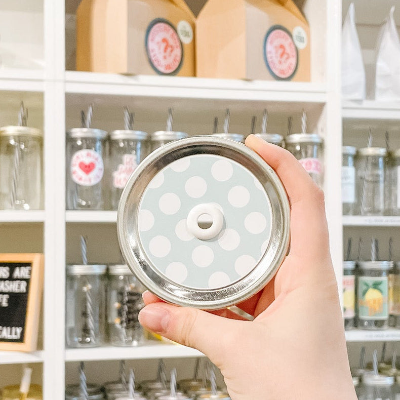 Hand holding mason jar straw lid that has large white polka dots on minty blue background