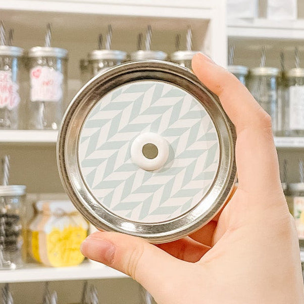 Hand holding mason jar patterned straw lid that has white chevron lines on minty blue background