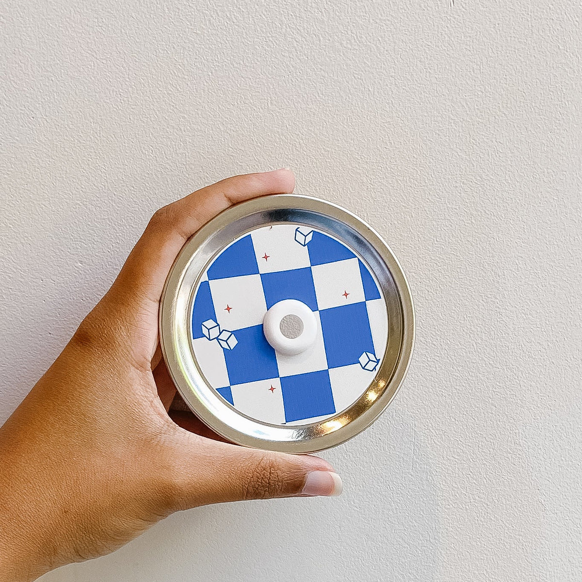 Hand holding mason jar straw lid that has white and blue checkered squares with small ice cube and red star designs