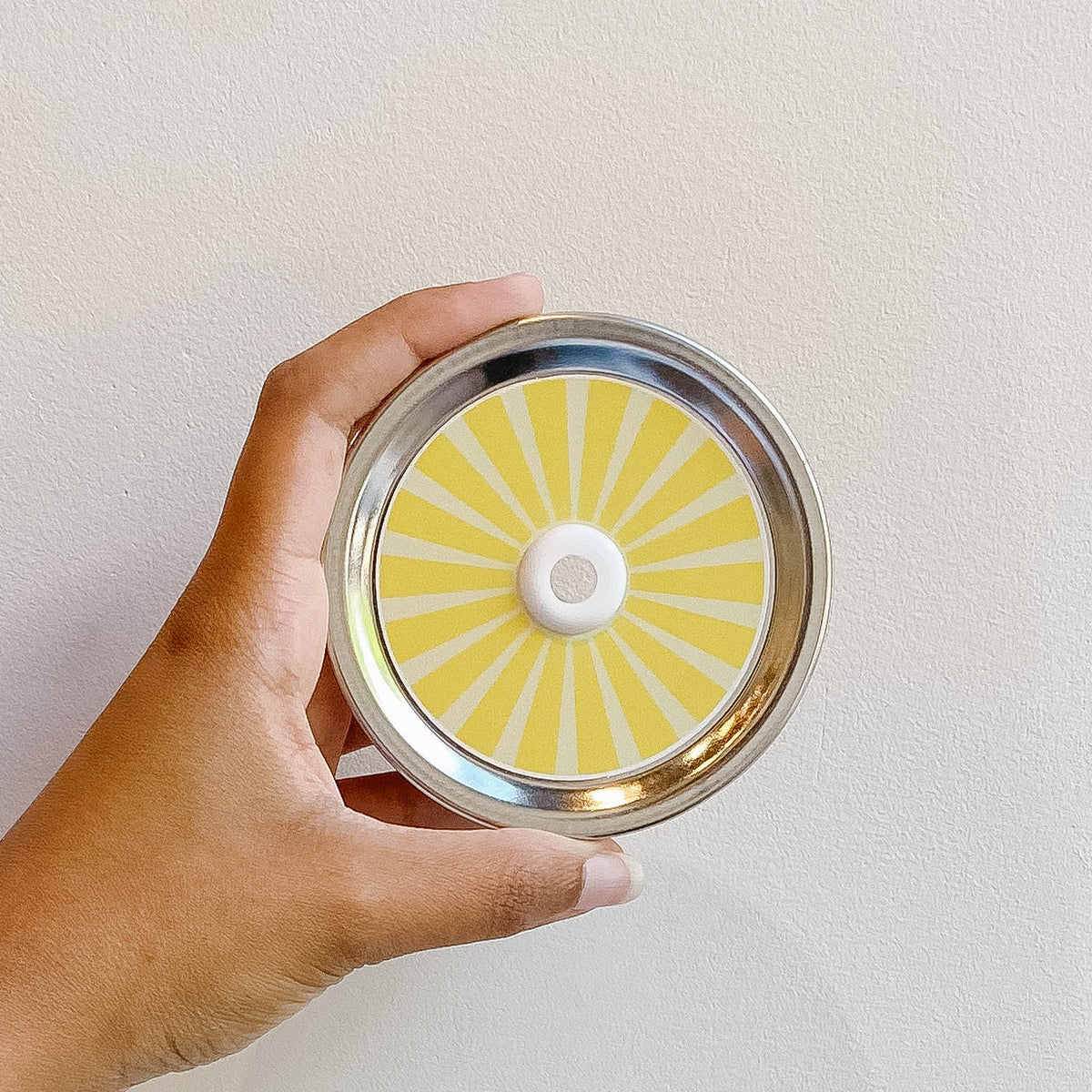 Hand holding mason jar patterned straw lid that has striped yellow design