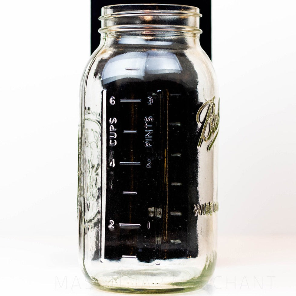 Side view of a Wide mouth half-gallon mason jar with Ball Wide mouth logo, and fruity oval design visible on the back side of the jar. against a white background