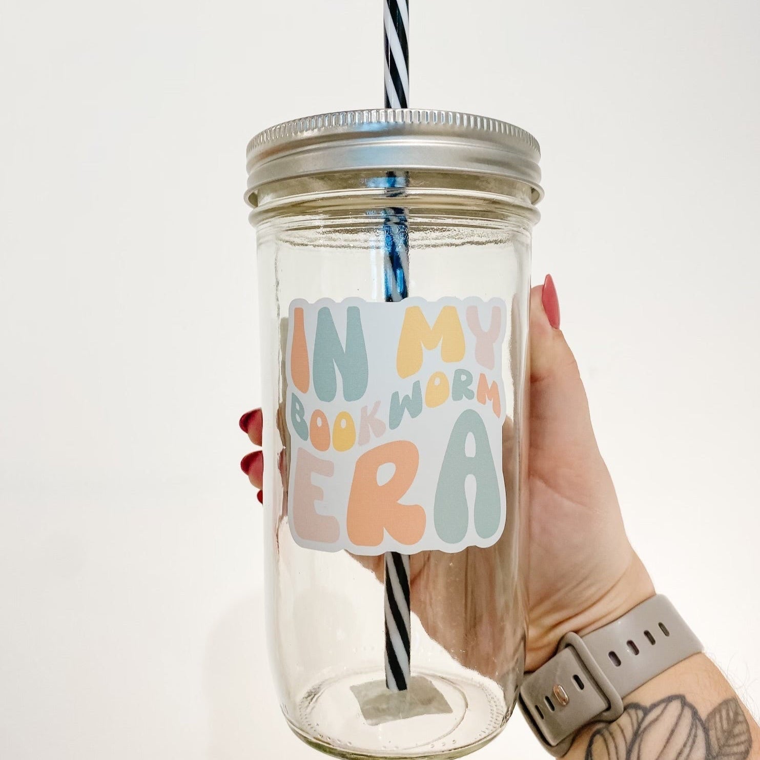hand holding a mason jar tumbler that reads "in my bookworm era" the lettering is bubbly and in different shades of yellow, orange, blue, and pink