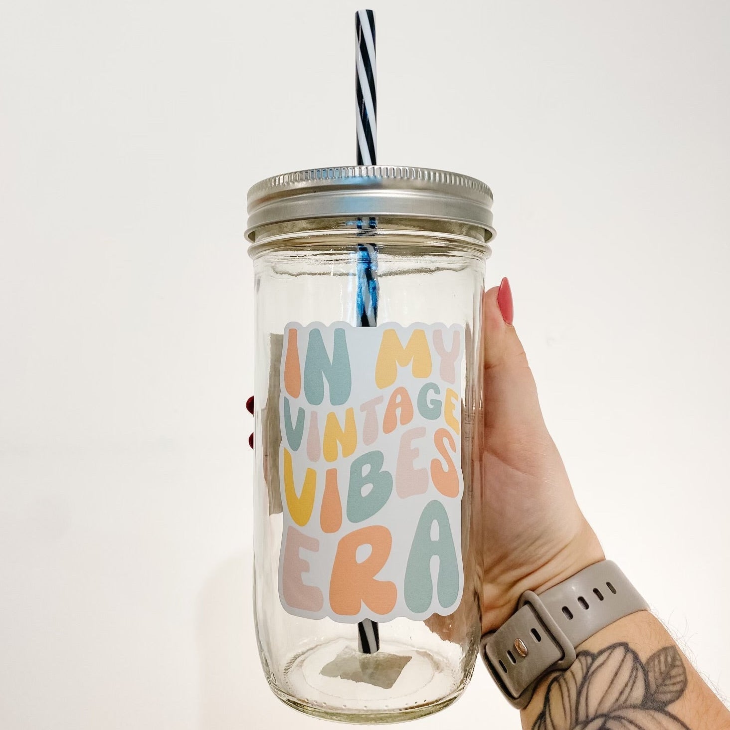hand holding a mason jar tumbler that says "in my vintage vibes era" the lettering is bubbly and in different shades of orange, yellow, pink, and blue