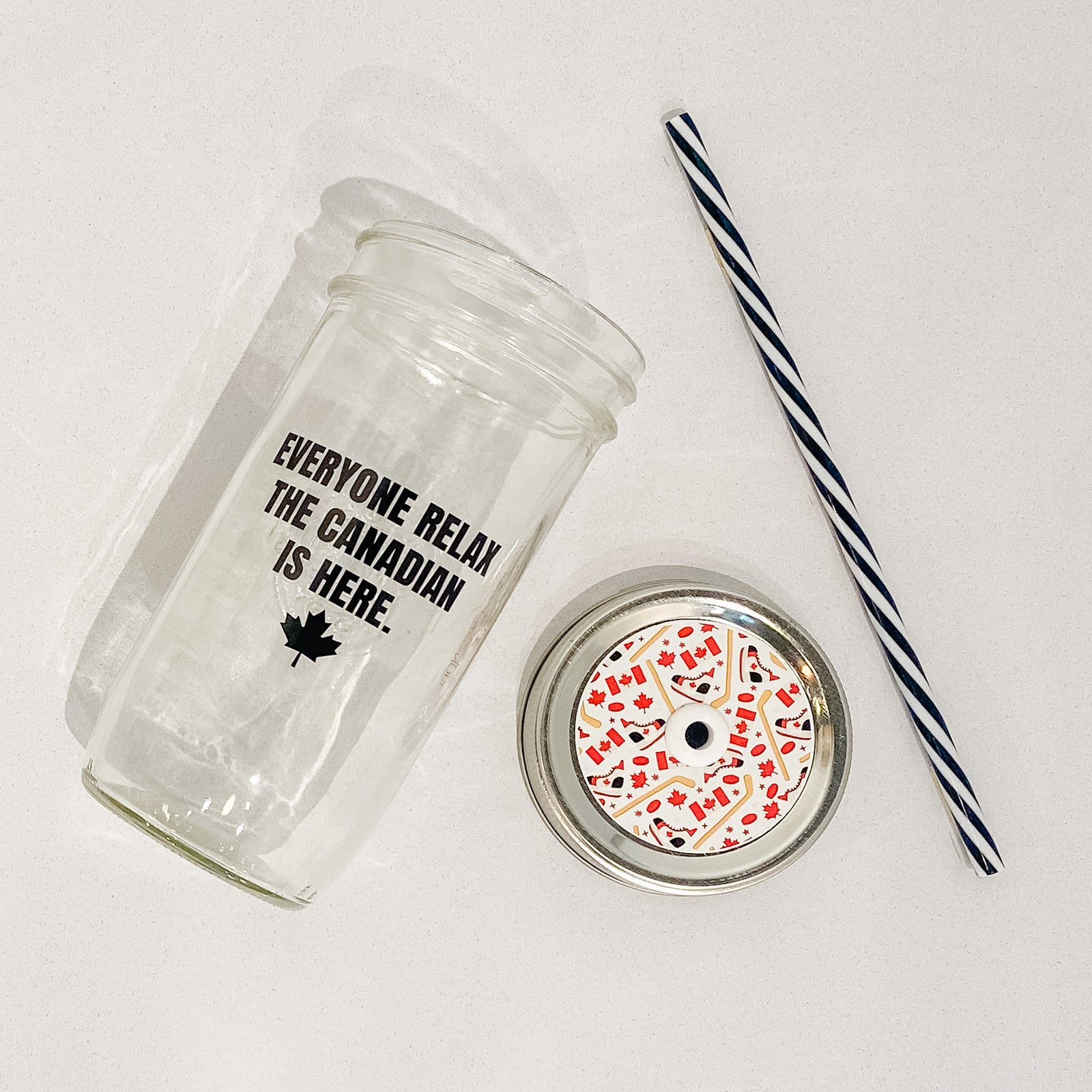 Hand holding mason jar that reads everyone relax the Canadian is here in black text. Small maple leaf at bottom.