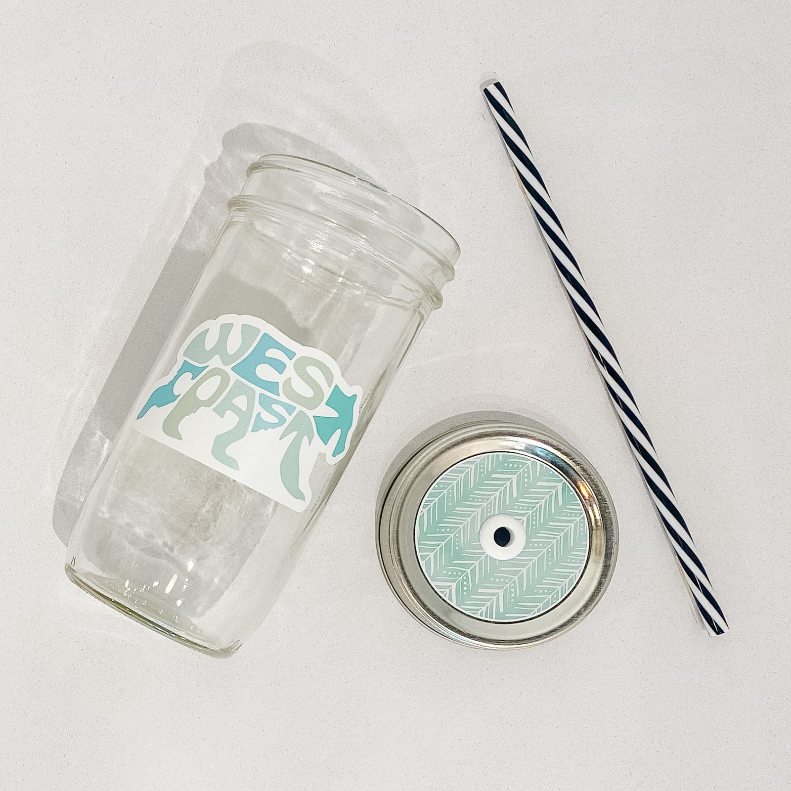 Hand holding mason jar tumbler that reads west coast in the shape of a bear. Multiple shades of blues/greens