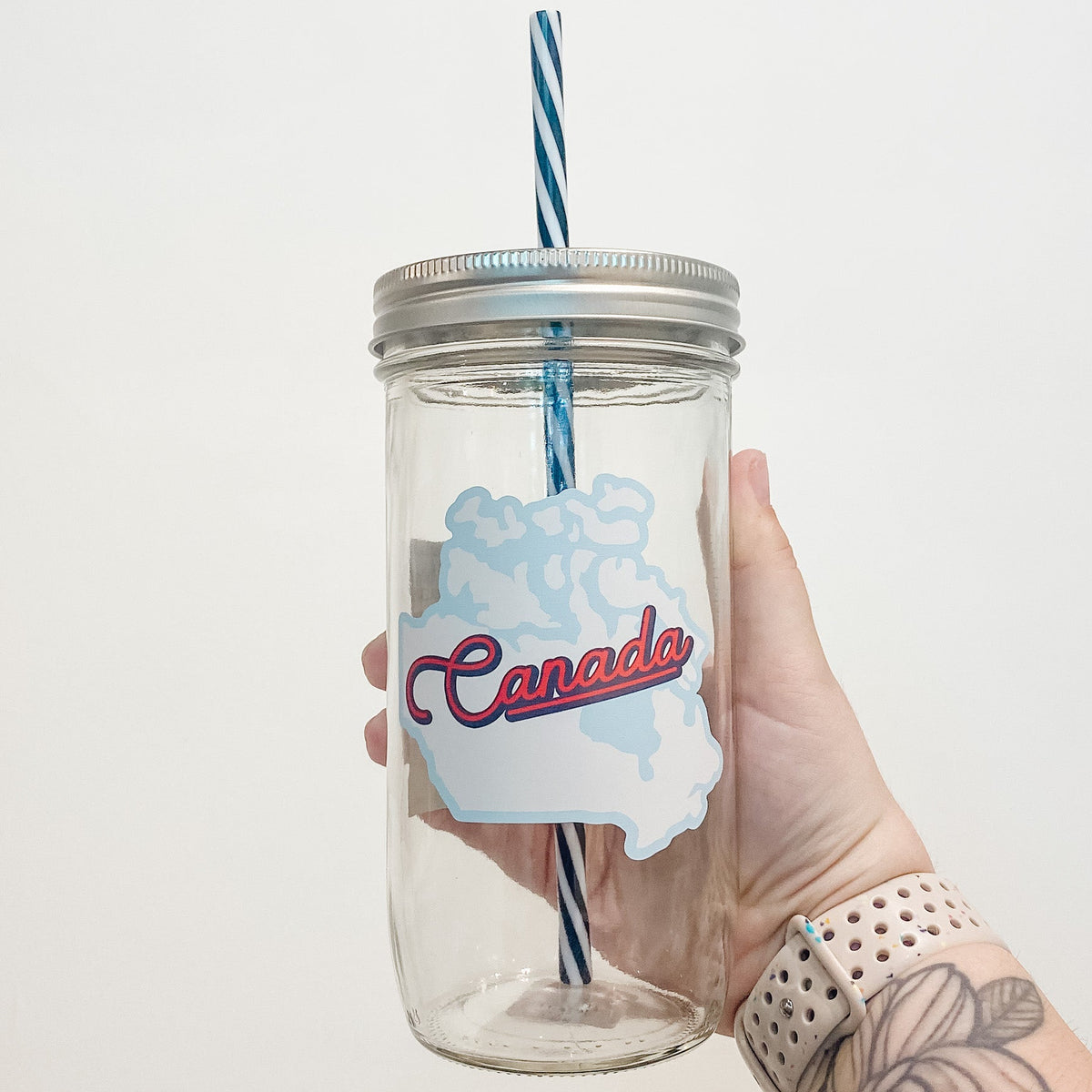 Hand holding mason jar that reads Canada in red surrounded by blue shape of Canada.