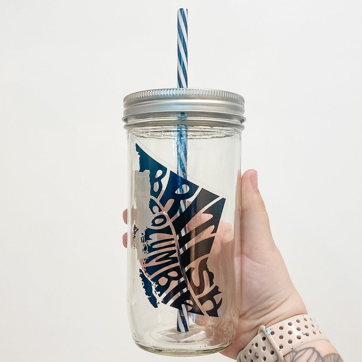 Hand holding mason jar that reads British Columbia in shape of province in black text and clear background.