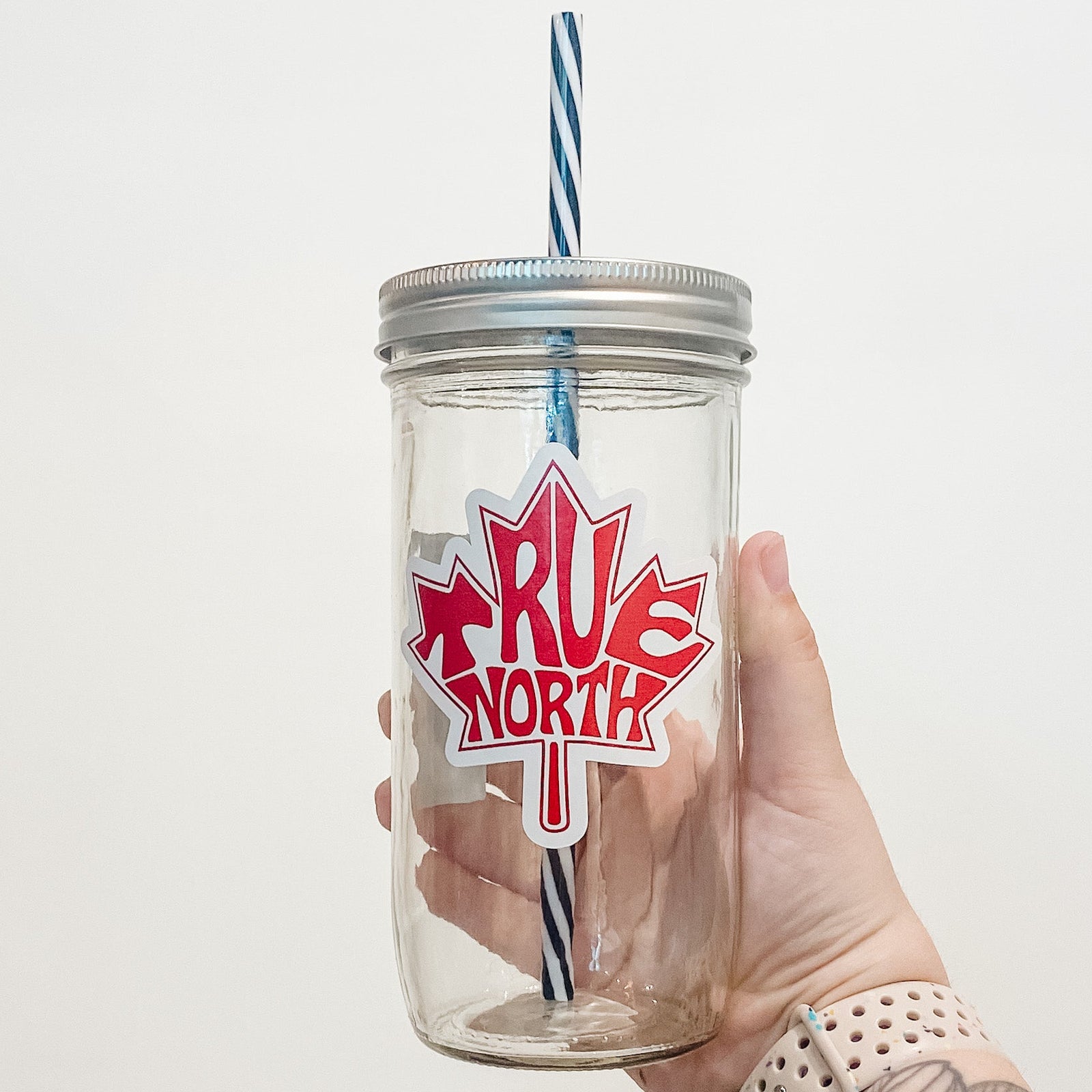 Hand holding mason jar that reads true north in the shape of a maple leaf
