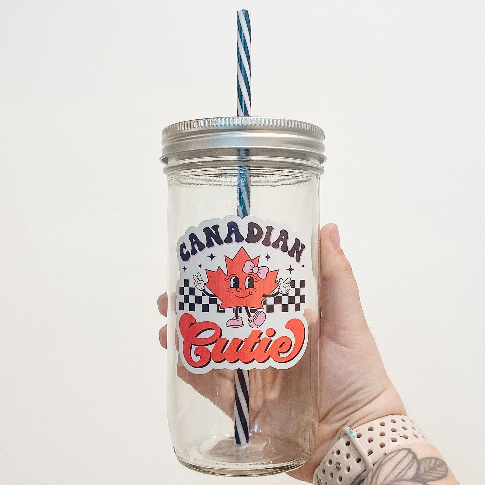 Hand holding mason jar that reads Canadian cutie in retro font with a animated maple leaf with pink shoes and pink bow.