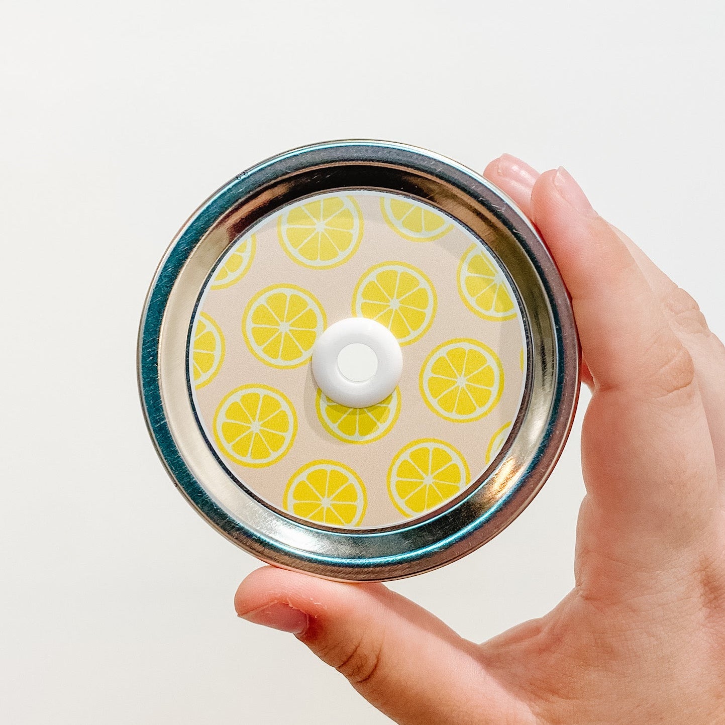 Hand holding a bright citrus patterned mason jar straw lid with orange and yellow design