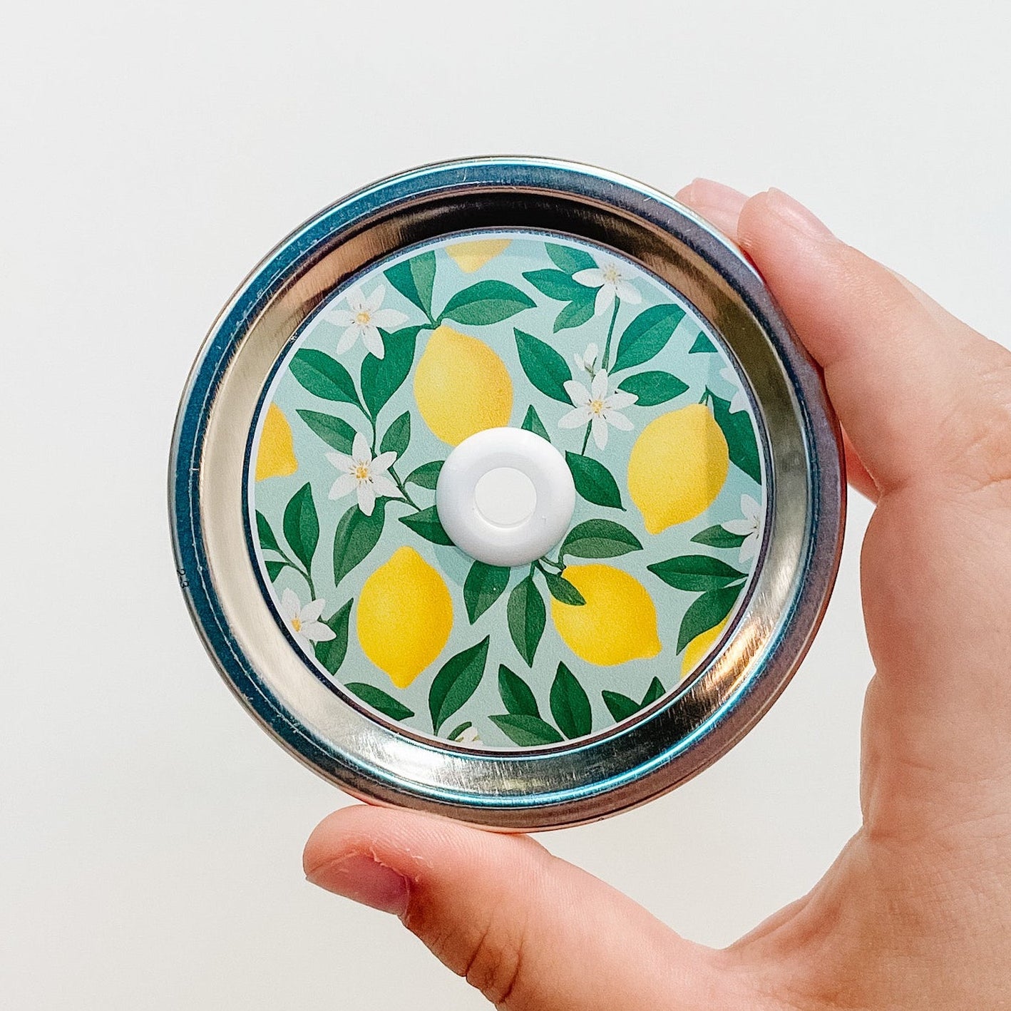 Hand holding a lemoncello yellow patterned mason jar straw lid with lemon design