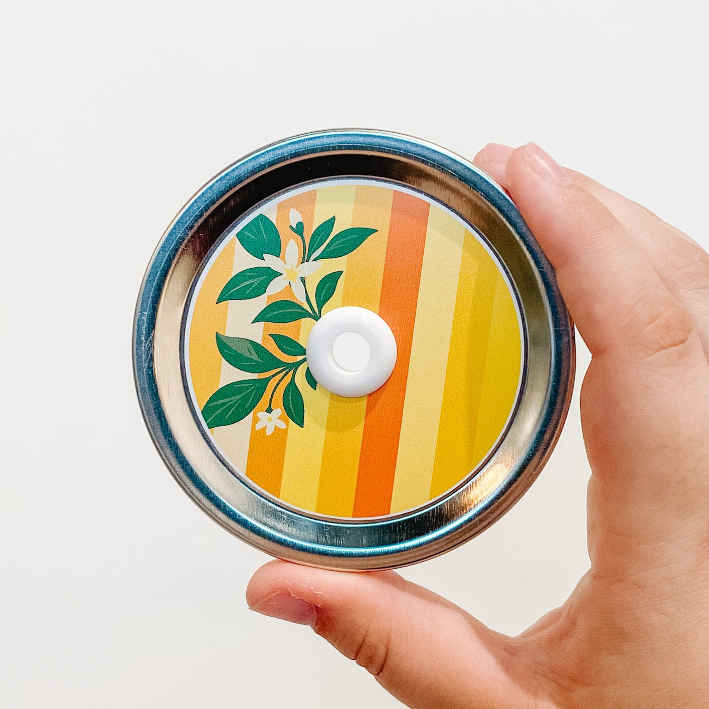 Hand holding a citrus zest patterned mason jar straw lid with lemon and orange design