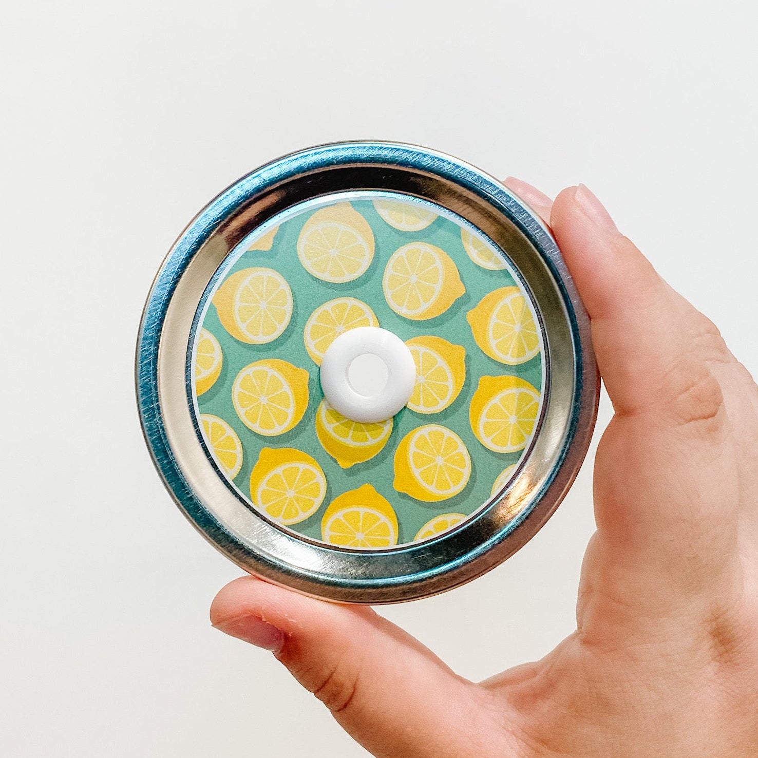 Hand holding a lemon squeeze patterned mason jar straw lid with yellow citrus design