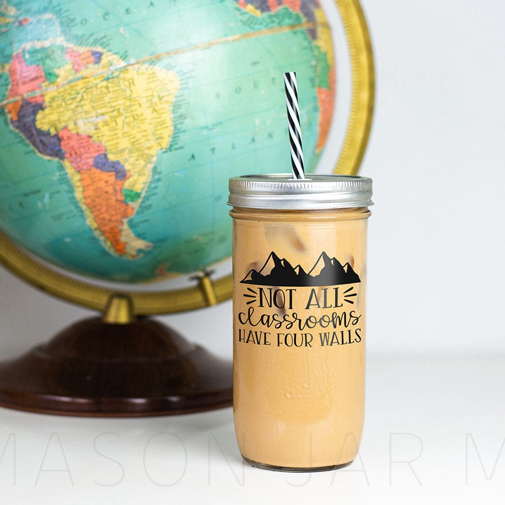 Tumbler with iced coffee with print "Not All Classrooms Have Four Walls" with mountains design. Photographed against a backdrop of a globe.