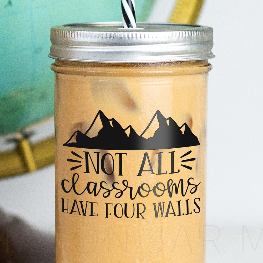 Zoomed in tumbler with iced coffee with sticker that says "Not All Classrooms Have Four Walls" with mountains above the text in the design.