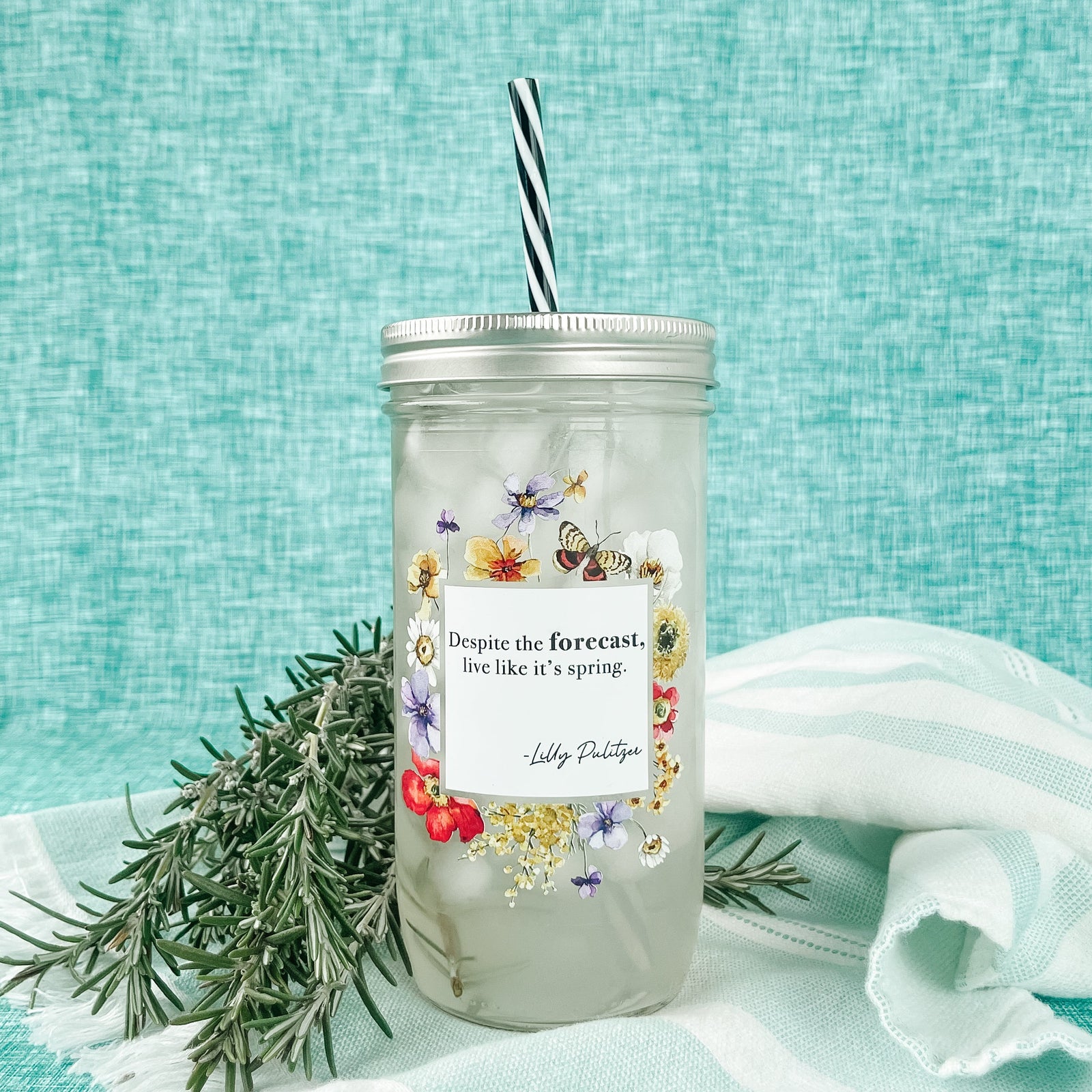 Mason jar tumbler that says “Despite the forecast, live like it’s spring. -Lilly Pulitzer” with flowers and butterflies creating a box around the words.