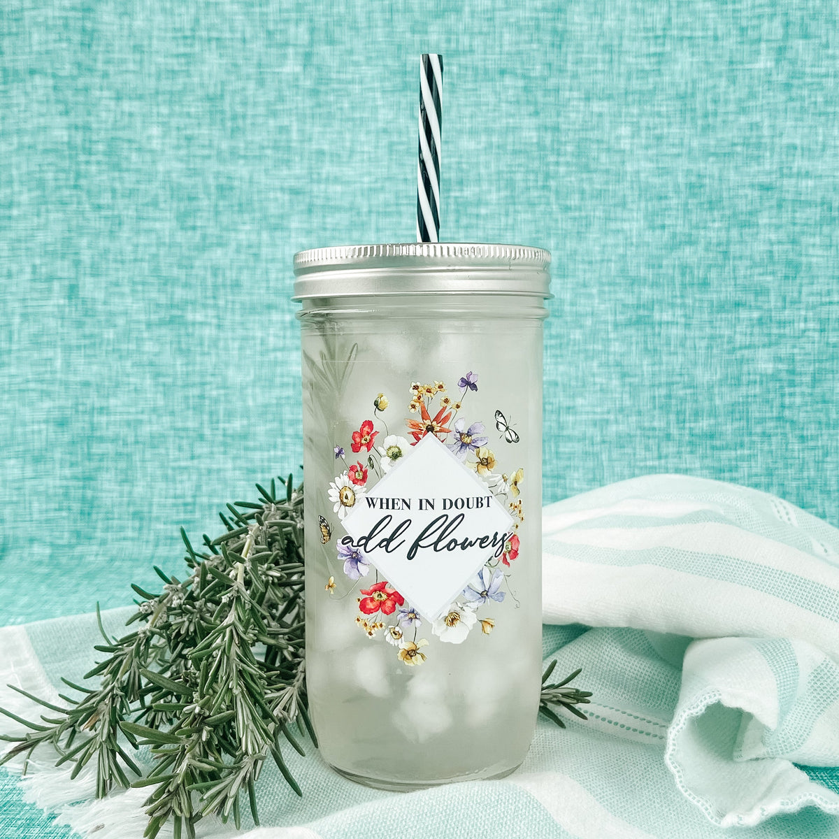 Mason jar tumbler that says “when in doubt add flowers” with flowers creating a diamond around the words.