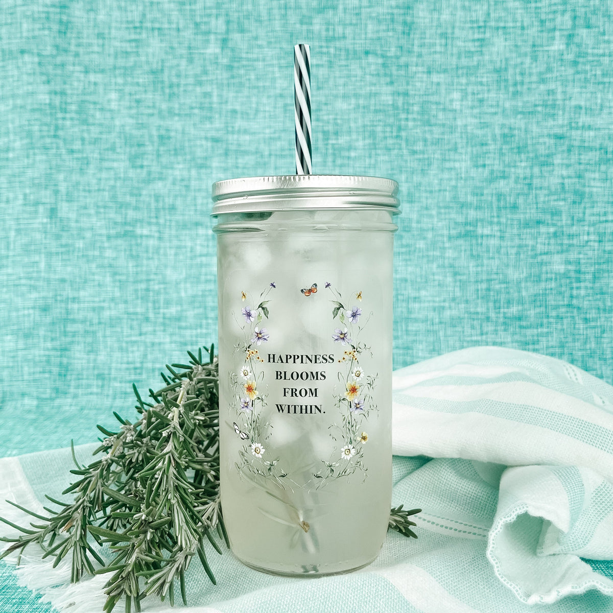 Mason jar tumbler that says “happiness blooms from within” with small flowers around the words.