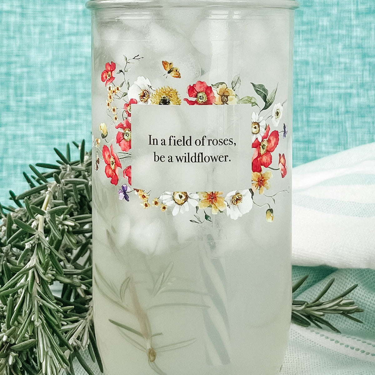 Close up of a mason jar tumbler that says “in a field of roses, be a wildflower” with flowers creating a rectangle around the words