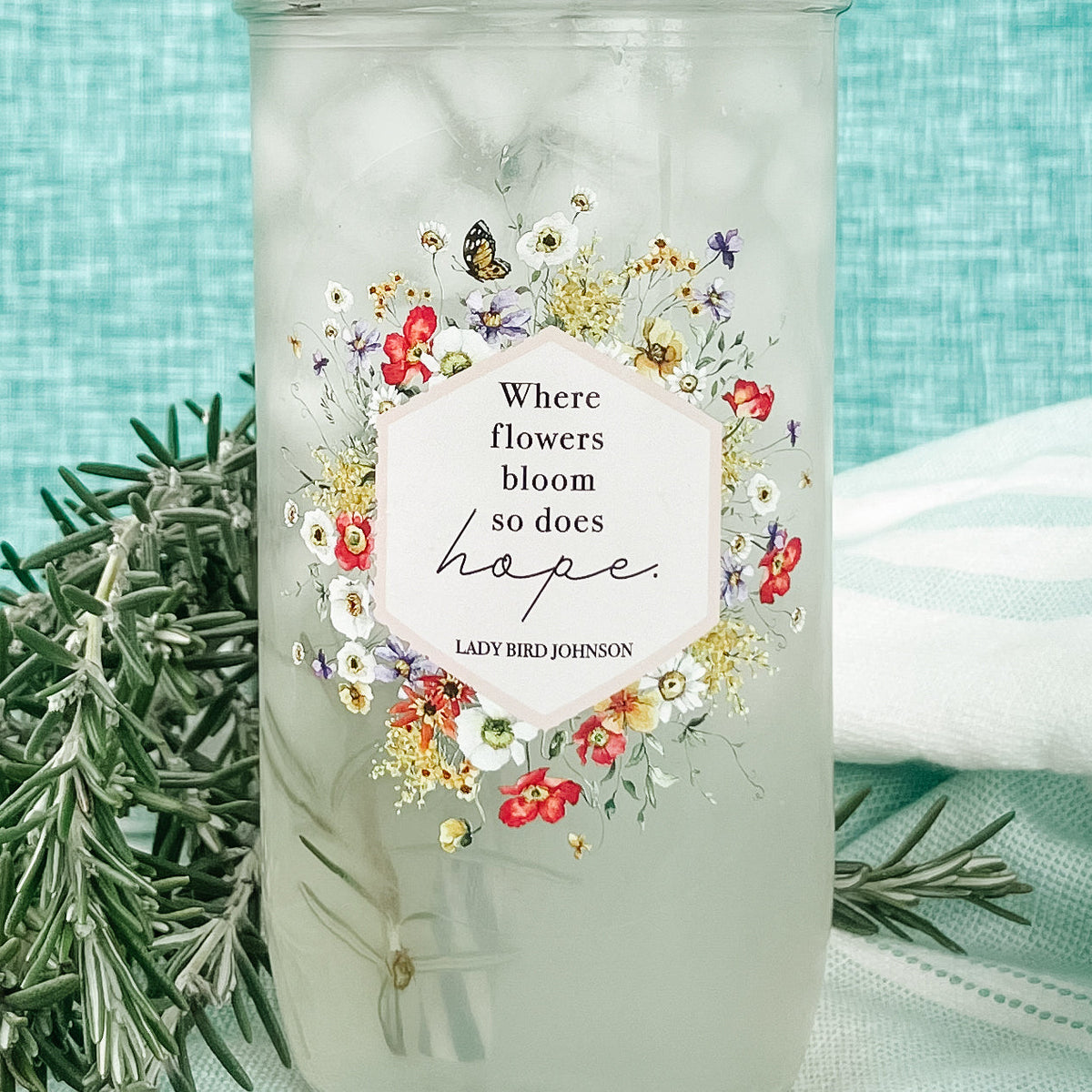 Close up of a mason jar tumbler that says “Where flowers bloom so does hope. Lady Bird Johnson” with flowers and butterflies creating a hexagon around the quote.