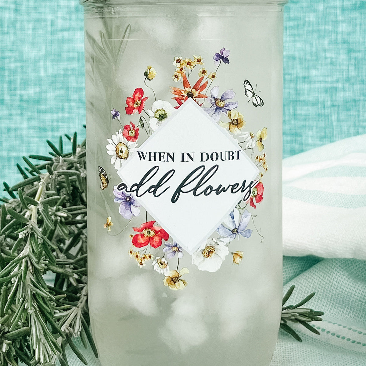 Close up of a mason jar tumbler that says “when in doubt add flowers” with flowers creating a diamond around the words.