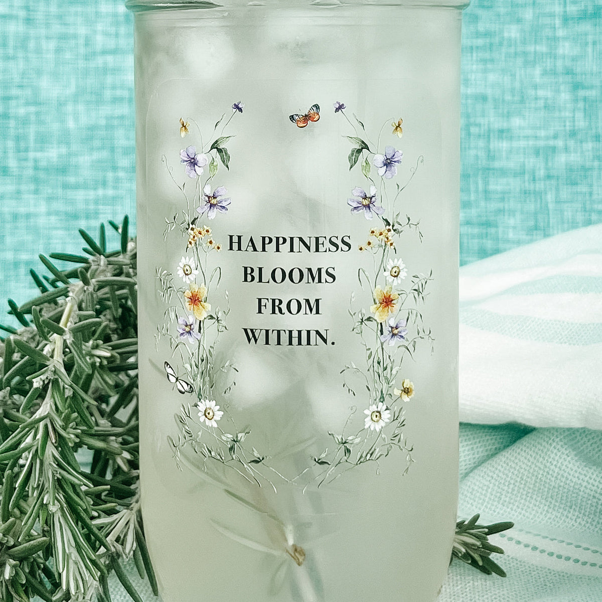Close up of a mason jar tumbler that says “happiness blooms from within” with small flowers around the words.